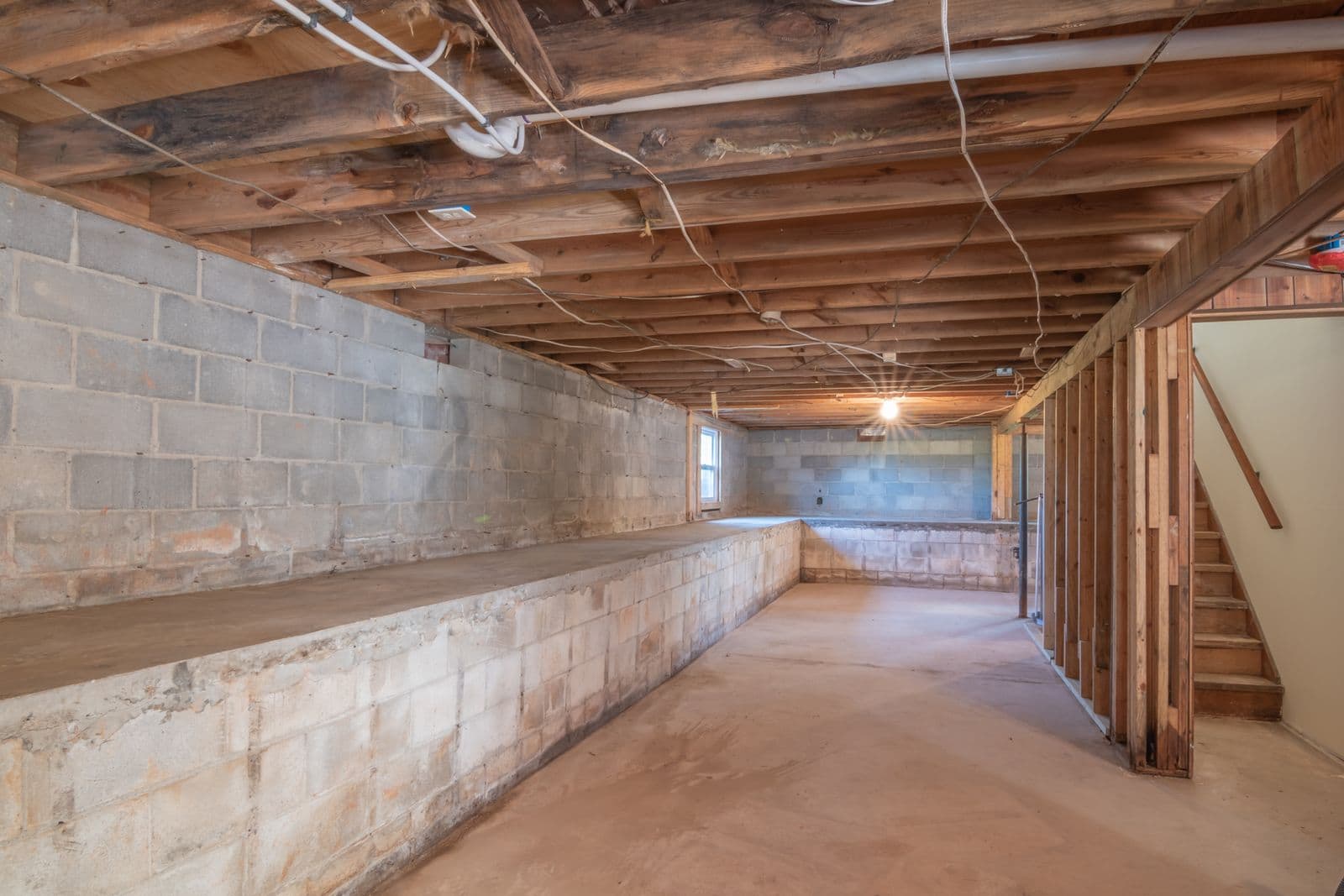 Empty basement with concrete walls, exposed beams and stairs
